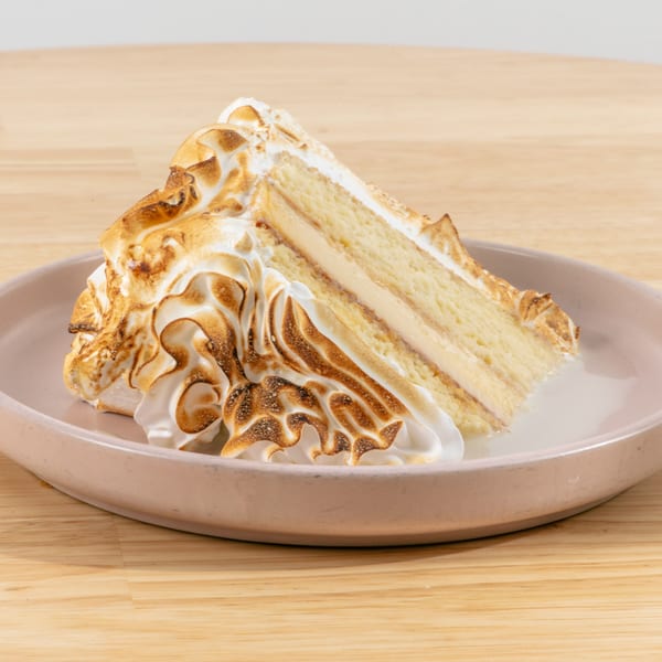 Slice of cake with toasted meringue topping and creamy filling on a pink plate.