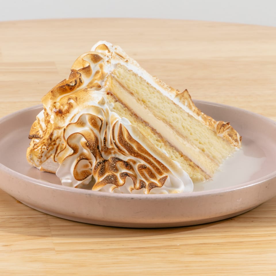 Slice of cake with toasted meringue topping and creamy filling on a pink plate.