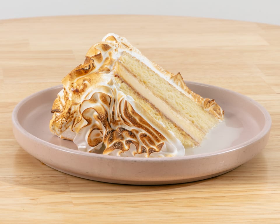Slice of cake with toasted meringue topping and creamy filling on a pink plate.