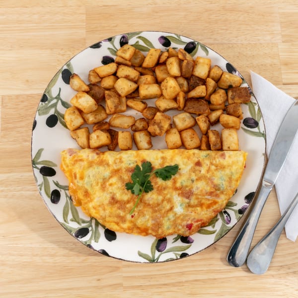Omelet with a sprig of parsley and a side of crispy home fries on an olive-patterned plate.