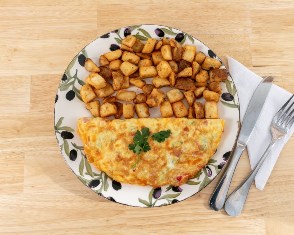 Omelet with a sprig of parsley and a side of crispy home fries on an olive-patterned plate.