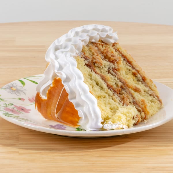 A slice of cake with white whipped cream and caramel filling on a floral plate.
