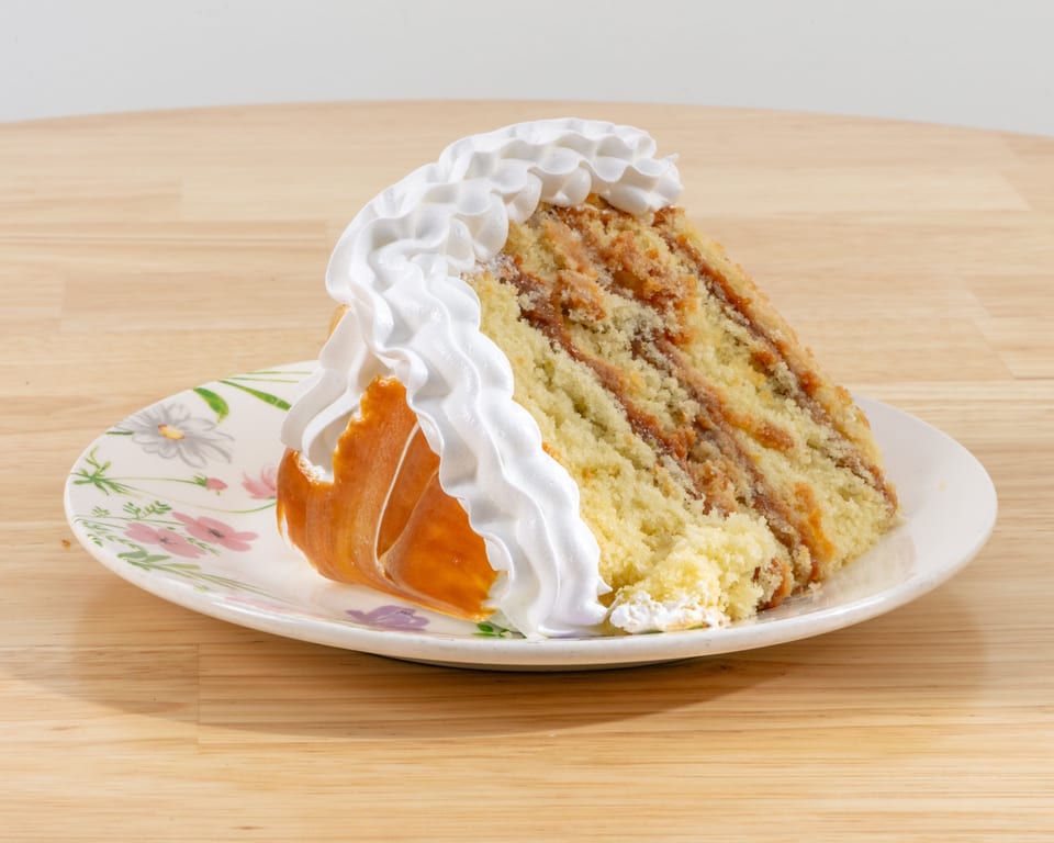A slice of cake with white whipped cream and caramel filling on a floral plate.