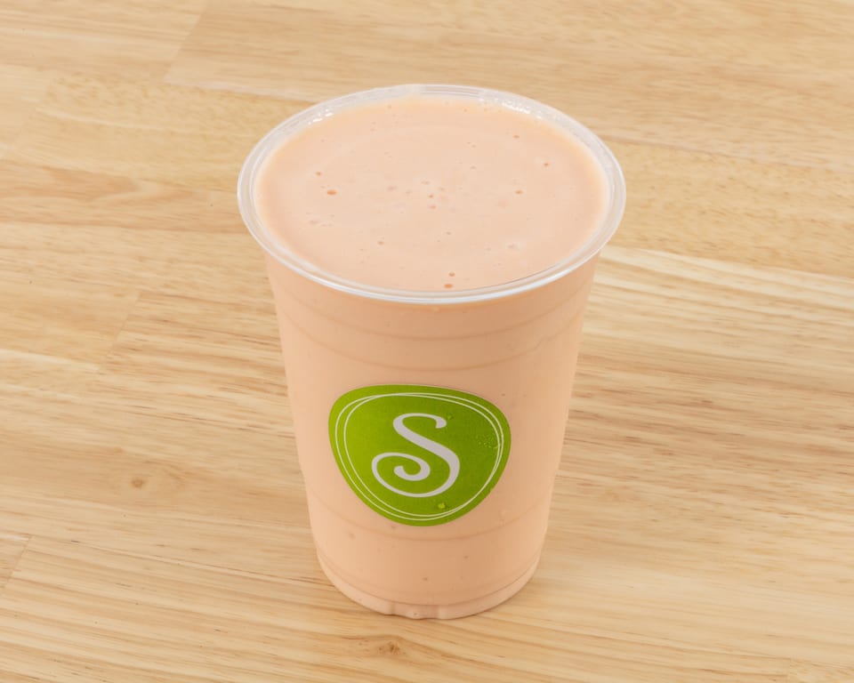 A peach-colored smoothie in a clear plastic cup with a green "S" logo on a wooden surface.