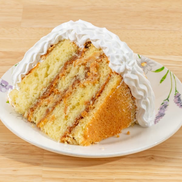 Slice of vanilla cake with dulce de leche filling and whipped cream on a floral plate.
