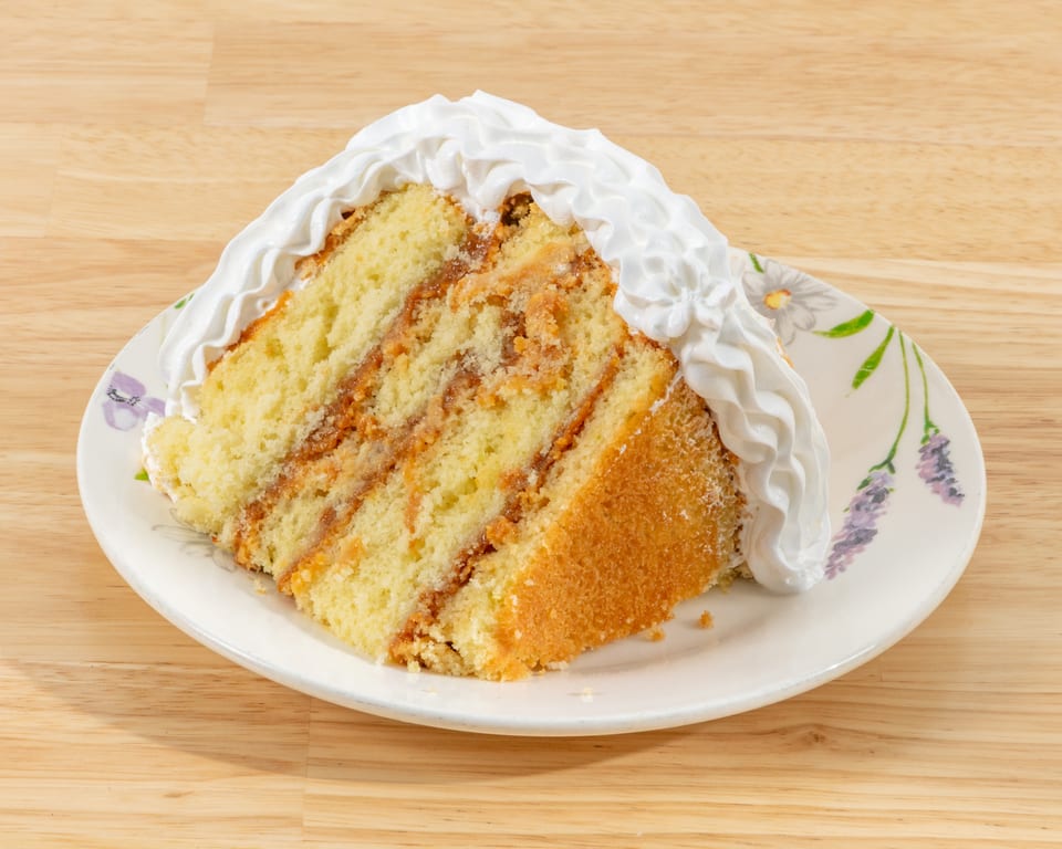 Slice of vanilla cake with dulce de leche filling and whipped cream on a floral plate.