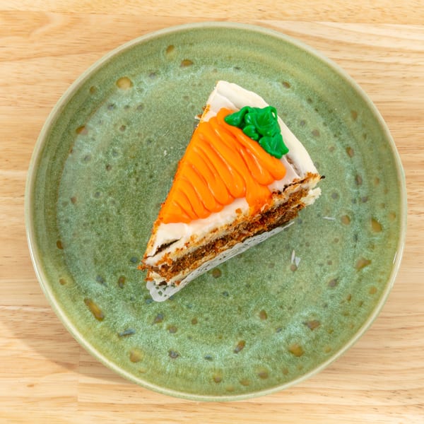 A slice of carrot cake with white frosting and an orange and green carrot decoration on a green plate.