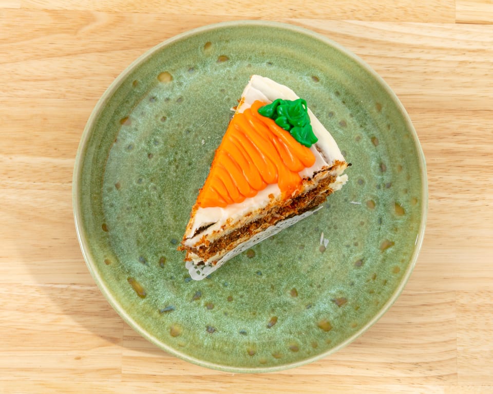 A slice of carrot cake with white frosting and an orange and green carrot decoration on a green plate.
