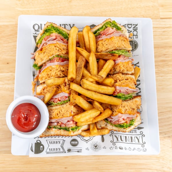 Club sandwiches with fries and ketchup on a white plate with patterned paper.