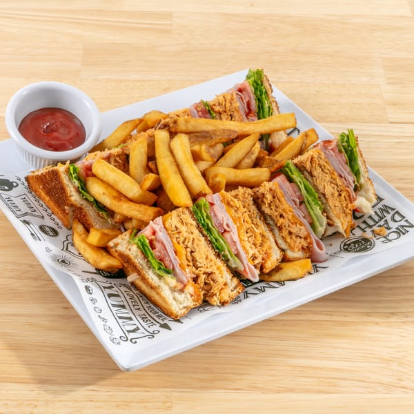 Club sandwiches with ham, chicken, lettuce, and tomato, served with fries and ketchup on a white plate.