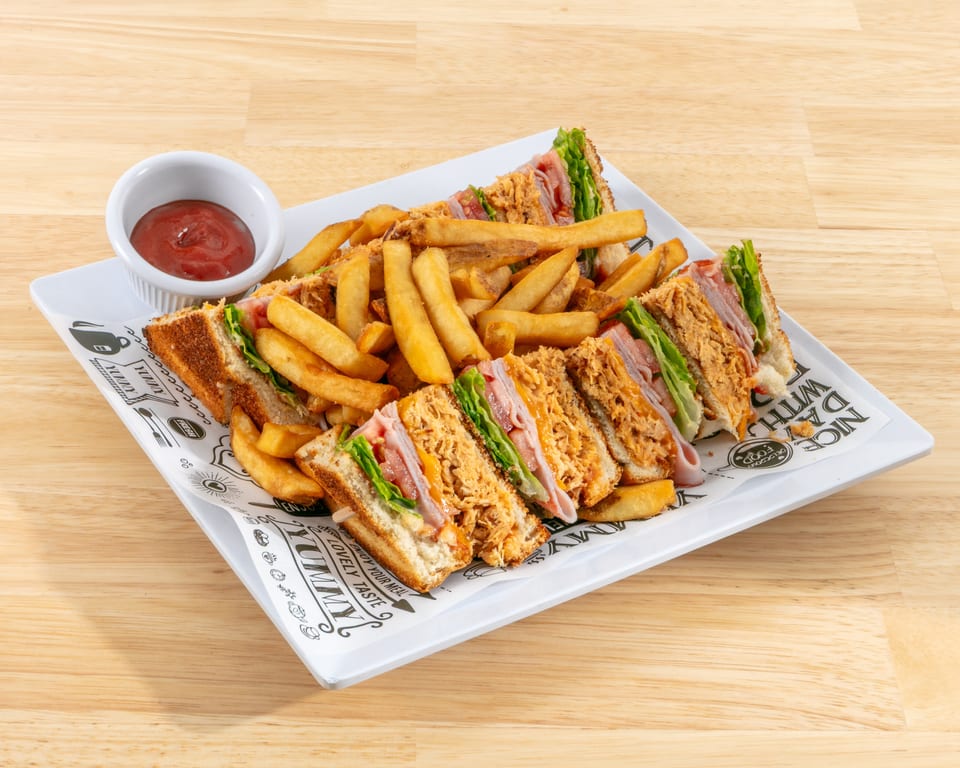 Club sandwiches with ham, chicken, lettuce, and tomato, served with fries and ketchup on a white plate.