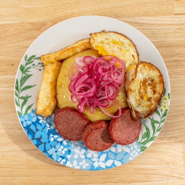 Mangu with fried eggs, salami, fried cheese, and pickled red onions on a floral plate.