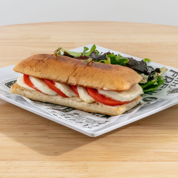 Caprese sandwich with mozzarella, tomato, and basil on ciabatta bread, served with a side salad.