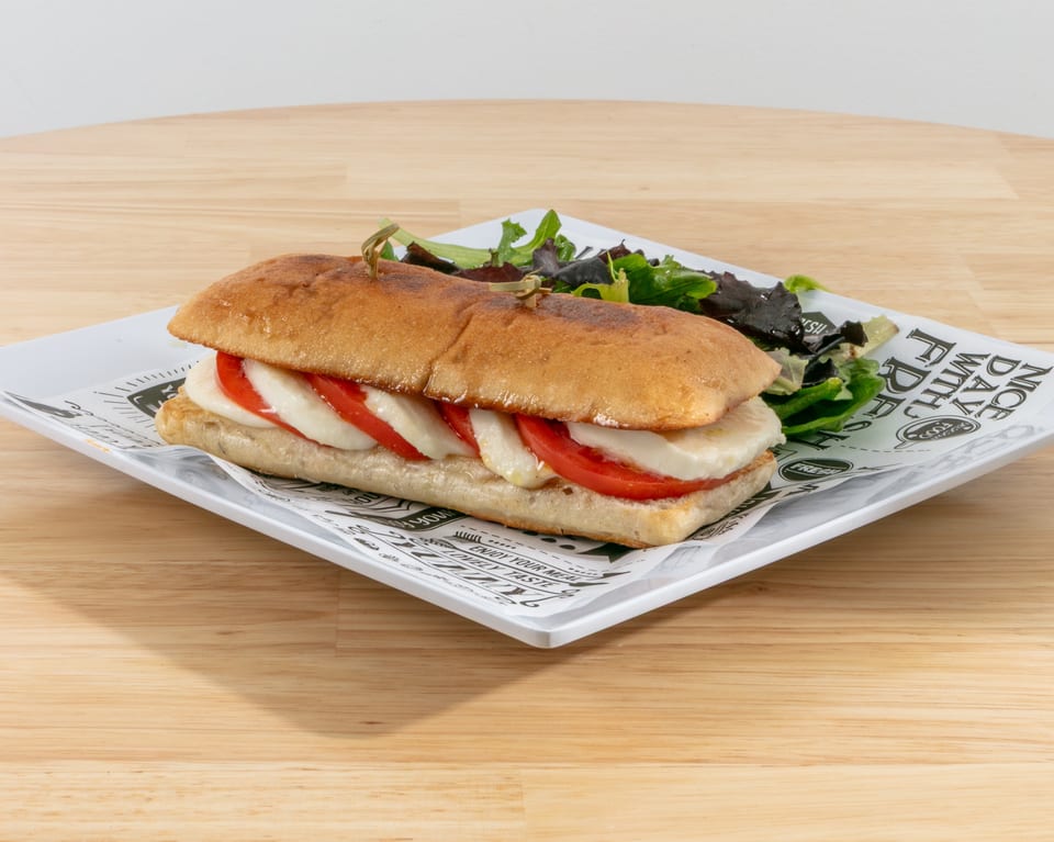 Caprese sandwich with mozzarella, tomato, and basil on ciabatta bread, served with a side salad.