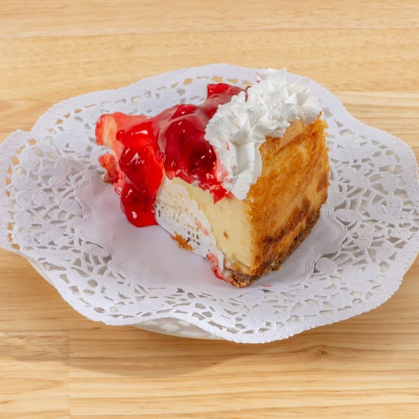 Slice of cheesecake topped with cherry pie filling and whipped cream on a white doily.