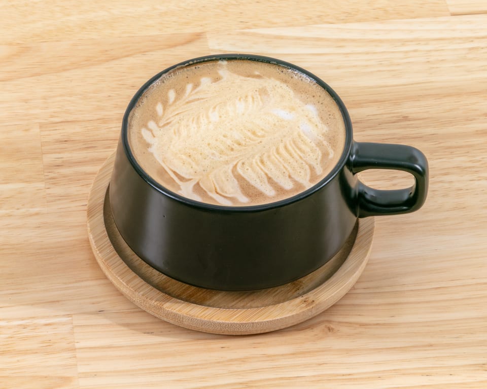 A black mug of latte with intricate foam art sits on a wooden coaster and table.