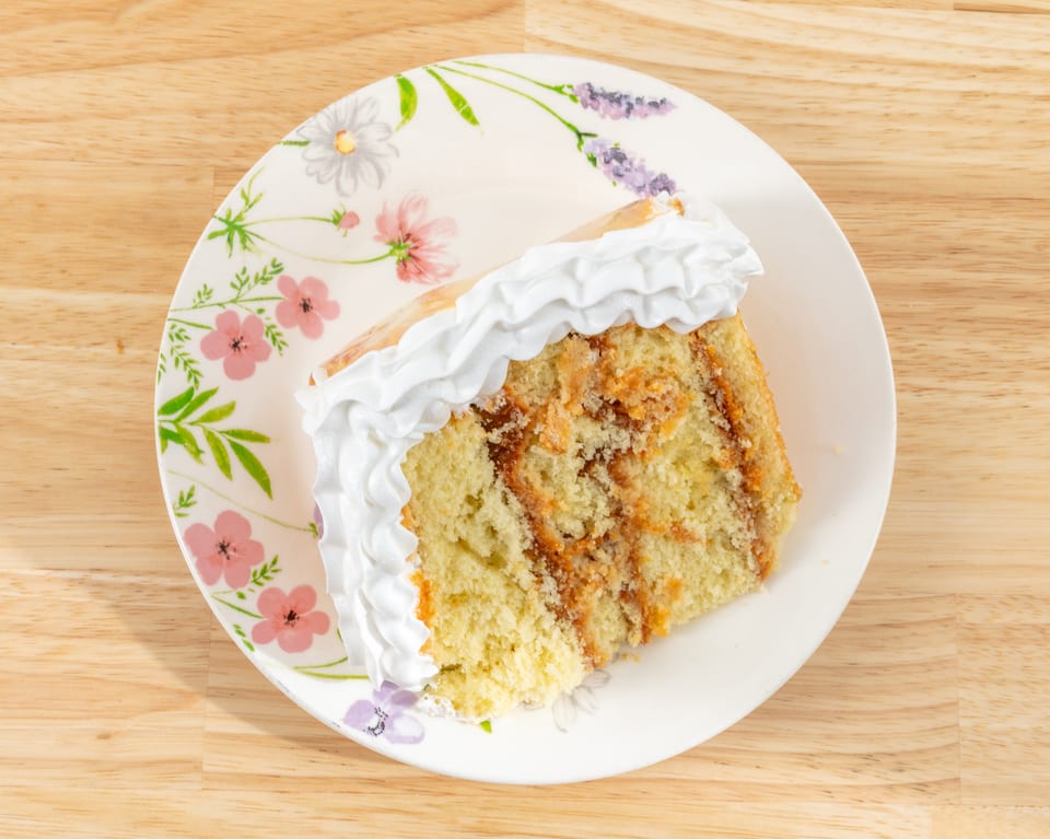 Slice of cake with white frosting and caramel swirls on a floral plate.